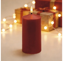 Rote LED-Stumpenkerze in einer festlichen Dekoration mit Geschenken und einer hellen Lichterkette.