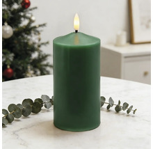 Dunkelgrüne LED-Stumpenkerze mit flackernder Flamme auf hellem Tisch mit Eukalyptuszweig in einem hellen, weihnachtlichen Raum.