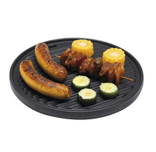 Runde, schwarze Grillplatte aus Gusseisen mit Riffeln, belegt mit Würstchen, Fleischspieß, Mais und Zucchini.