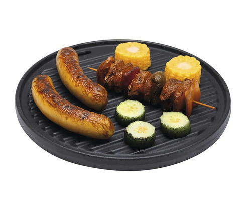 Runde, schwarze Grillplatte aus Gusseisen mit Riffeln, belegt mit Würstchen, Fleischspieß, Mais und Zucchini.
