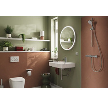 Modernes Badezimmer mit wandhängender Toilette, Waschbecken, rundem LED-Spiegel und Dusche. Wandgestaltung in Grün und Terrakotta.