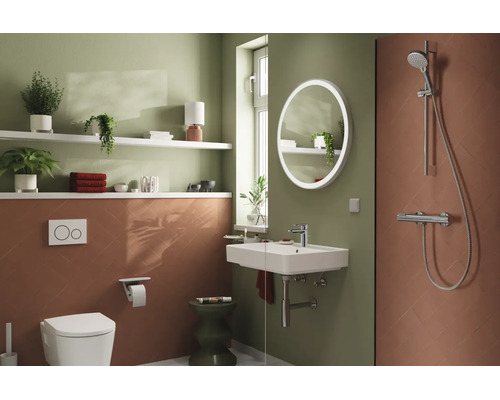 Modernes Badezimmer mit wandhängender Toilette, Waschbecken, rundem LED-Spiegel und Dusche. Wandgestaltung in Grün und Terrakotta.