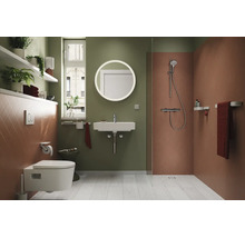Modernes Badezimmer mit wandhängendem WC, Waschbecken, rundem Spiegel, ebenerdiger Dusche, Regalen und Zimmerpflanzen.