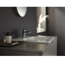 Moderne Badezimmerszene mit einer eleganten Waschtischarmatur auf einem Keramikwaschbecken, einem runden Spiegel und einem Waschtischunterschrank.
