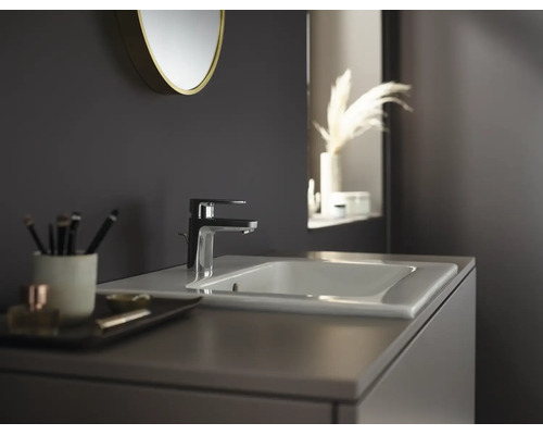 Moderne Badezimmerszene mit einer eleganten Waschtischarmatur auf einem Keramikwaschbecken, einem runden Spiegel und einem Waschtischunterschrank.