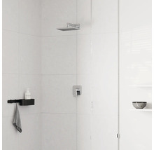 Douche moderne avec pomme de douche carrée en chrome, mitigeur monocommande et étagère de douche noire sur mur carrelé clair.