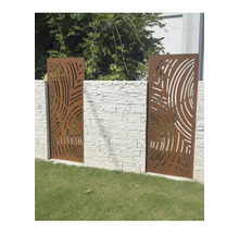 Panneaux de clôture décoratifs en métal aspect rouille avec découpes circulaires, montés sur un mur en pierre claire dans un jardin.