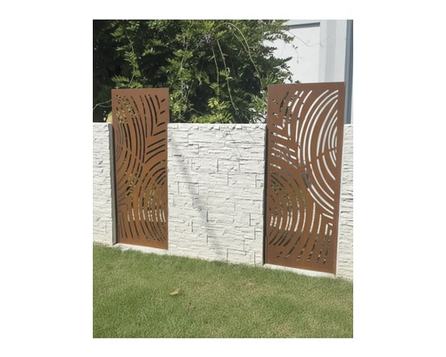 Panneaux de clôture décoratifs en métal aspect rouille avec découpes circulaires, montés sur un mur en pierre claire dans un jardin.