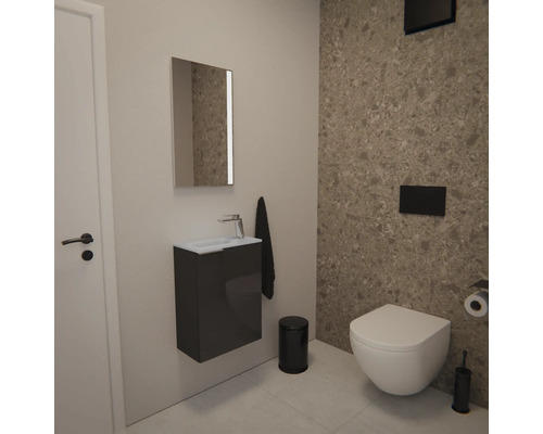 Modernes Gäste-WC mit wandhängendem WC, grauem Waschtischunterschrank mit kleinem Waschbecken, Spiegel und schwarzen Accessoires vor Steinwand.