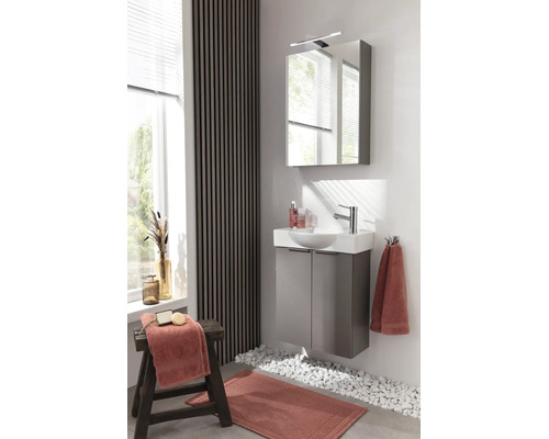 Modernes helles Badezimmer mit grauem Waschbeckenunterschrank, weißem Waschbecken, Spiegelschrank mit Leuchte und Wand mit Holzlamellen.