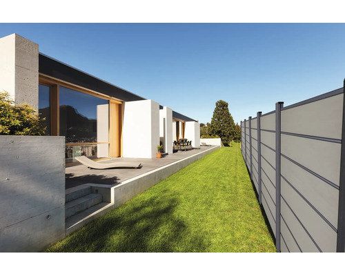 Moderner Sichtschutzzaun aus Paneelen neben Rasenfläche und Terrasse eines zeitgenössischen Hauses mit großen Glasfronten.