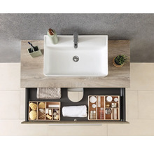 Meuble sous-vasque moderne aspect bois avec vasque à poser blanche et tiroir ouvert contenant des articles de salle de bain et serviettes organisés.