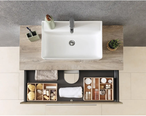 Meuble sous-vasque moderne aspect bois avec vasque à poser blanche et tiroir ouvert contenant des articles de salle de bain et serviettes organisés.