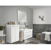Salle de bain moderne avec meuble sous-vasque blanc à deux tiroirs, armoire haute assortie, miroir avec éclairage et papier peint gris à motifs.