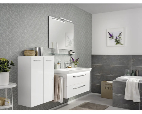 Salle de bain moderne avec meuble sous-vasque blanc à deux tiroirs, armoire haute assortie, miroir avec éclairage et papier peint gris à motifs.