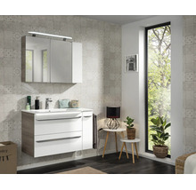 Ensemble de salle de bain blanc avec meuble sous-vasque, vasque en céramique et armoire miroir devant carrelage gris clair, ambiance lumineuse.