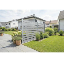 Clôture brise-vue moderne avec lattes horizontales grises dans un jardin soigné avec terrasse, pelouse et bacs à fleurs.