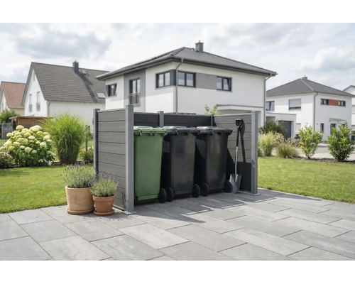 Cache-poubelle moderne gris en matériau composite sur une terrasse dans un jardin organisé avec des maisons en arrière-plan.