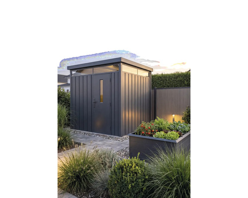 Abri de jardin moderne en métal avec toit plat et impostes dans un jardin aménagé avec un carré potager surélevé et un chemin en pierre.