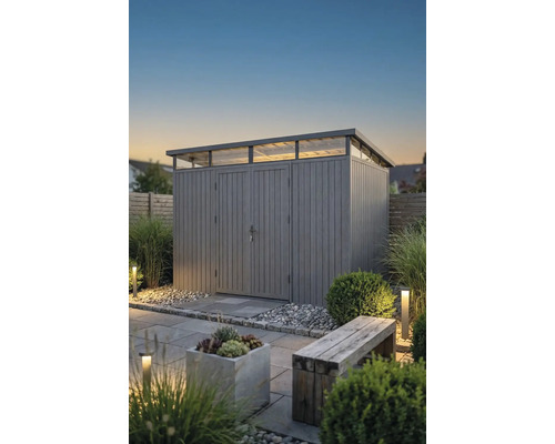 Modernes Gartenhaus mit Pultdach und Oberlichtern in einem Garten mit Steinplatten, Kies, Pflanzen und Außenbeleuchtung in der Dämmerung.
