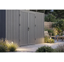Abri de jardin moderne gris en métal avec double porte sur une terrasse en pierre avec éclairage extérieur.