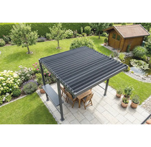 Pergola autoportante avec toit à lames sur une terrasse claire dans un jardin, avec meubles en bois, bassin et abri de jardin au fond.