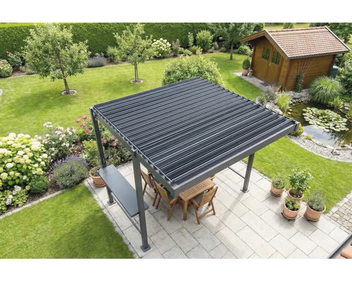 Pergola autoportante avec toit à lames sur une terrasse claire dans un jardin, avec meubles en bois, bassin et abri de jardin au fond.