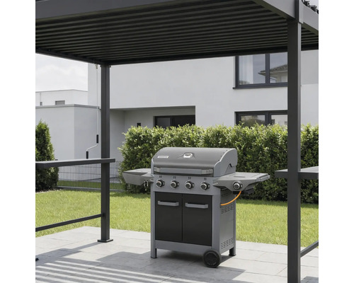 Barbecue à gaz avec quatre brûleurs et tablettes latérales sur une terrasse pavée sous une pergola moderne en métal dans un jardin.