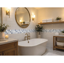 Salle de bain moderne et lumineuse avec baignoire en îlot, miroir rond, meubles en bois, carreaux métro et bordure en mosaïque.