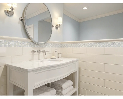 Salle de bains lumineuse avec meuble sous vasque blanc, plan en marbre, miroir ovale et carrelage mural type métro.