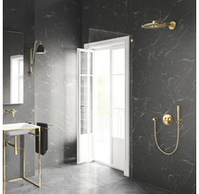 Modernes Badezimmer mit dunklen Marmorfliesen, goldenen Duscharmaturen, Glaswand und weißem Waschbecken mit Goldgestell.
