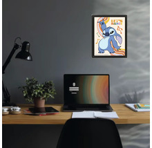 Poster encadré avec Stitch de Disney et texte Let's Dance au-dessus d'un bureau avec ordinateur portable et lampe dans un espace de travail.