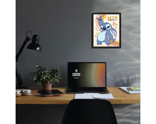 Poster encadré avec Stitch de Disney et texte Let's Dance au-dessus d'un bureau avec ordinateur portable et lampe dans un espace de travail.