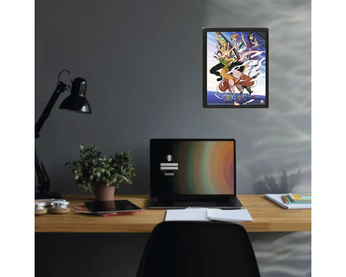 Poster One Piece encadré sur un mur au-dessus d'un bureau avec un ordinateur portable et une plante d'intérieur.