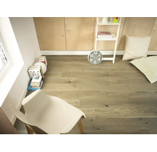 Pièce lumineuse avec parquet en chêne, chaise blanche, piles de livres et étagère blanche devant un mur lambrissé.