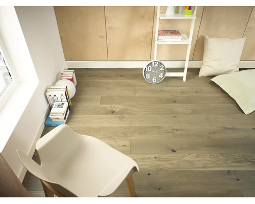 Pièce lumineuse avec parquet en chêne, chaise blanche, piles de livres et étagère blanche devant un mur lambrissé.