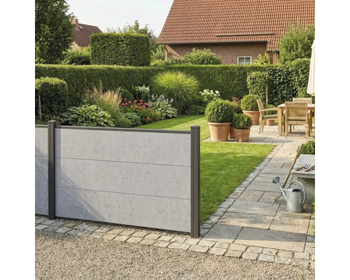 Clôture pare-vue moderne aspect béton dans un jardin avec pelouse, massifs et une terrasse pavée avec des meubles en bois.