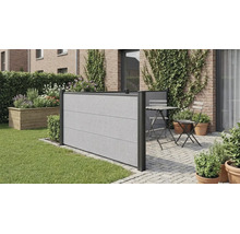 Brise-vue moderne aspect béton sur une terrasse pavée à côté d une pelouse, avec coin salon et mur en briques végétalisé.