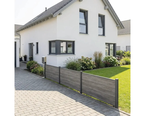 Clôture pare-vue moderne avec panneaux aspect bois et poteaux métalliques entre une allée pavée et une pelouse devant une maison blanche.