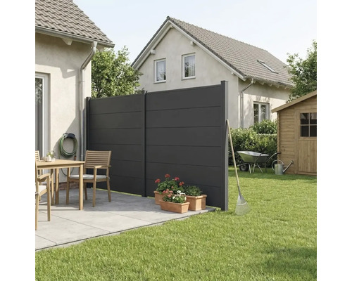 Brise-vue moderne de couleur anthracite composé de deux panneaux sur une terrasse carrelée à côté d'une pelouse et de meubles de jardin.