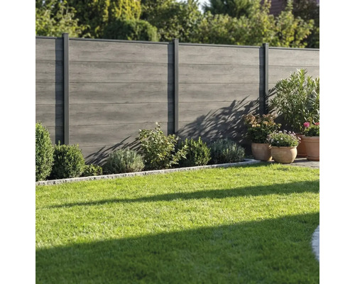 Clôture de jardin moderne grise en bois composite avec poteaux métalliques installée dans un jardin avec pelouse et arbustes.
