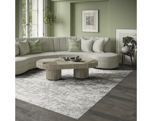 Modernes, helles Wohnzimmer mit einem großen grau-weiß gemusterten Teppich, einem geschwungenen cremefarbenen Sofa und einem hölzernen Couchtisch.
