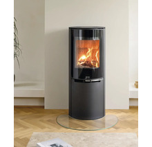 Moderner schwarzer Kaminofen mit brennendem Holzfeuer hinter einer großen Glasscheibe auf einer Glasbodenplatte in einem hellen Wohnraum.