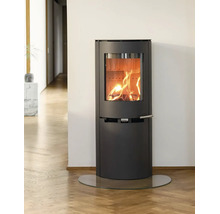 Moderner Kaminofen aus dunklem Metall mit loderndem Feuer in hellem Zimmer auf Parkettboden und einer Glasplatte.