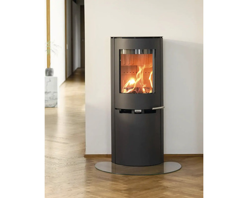 Moderner Kaminofen aus dunklem Metall mit loderndem Feuer in hellem Zimmer auf Parkettboden und einer Glasplatte.