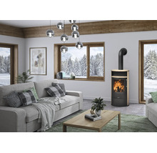 Poêle à bois moderne en métal noir et bois dans un salon lumineux avec un canapé gris et de grandes fenêtres donnant sur les montagnes.