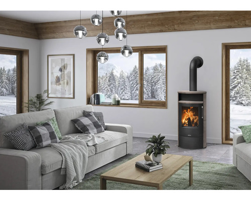 Poêle à bois moderne dans un salon lumineux avec vue sur un paysage hivernal enneigé à travers une grande fenêtre en bois.