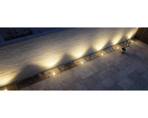 Des spots encastrés dans le sol éclairent un mur en pierre texturé sur une terrasse en dalles de pierre.