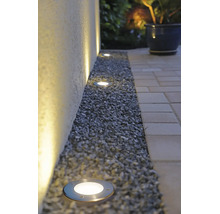 Spots encastrés de sol LED extérieurs dans un lit de gravier le long d'un mur, éclairant vers le haut avec une lumière blanche chaude.