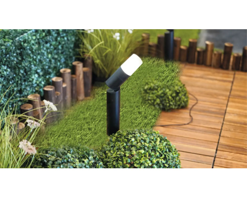 Lampe de jardin noire moderne sur du gazon synthétique près de la terrasse en bois dans un jardin lumineux.